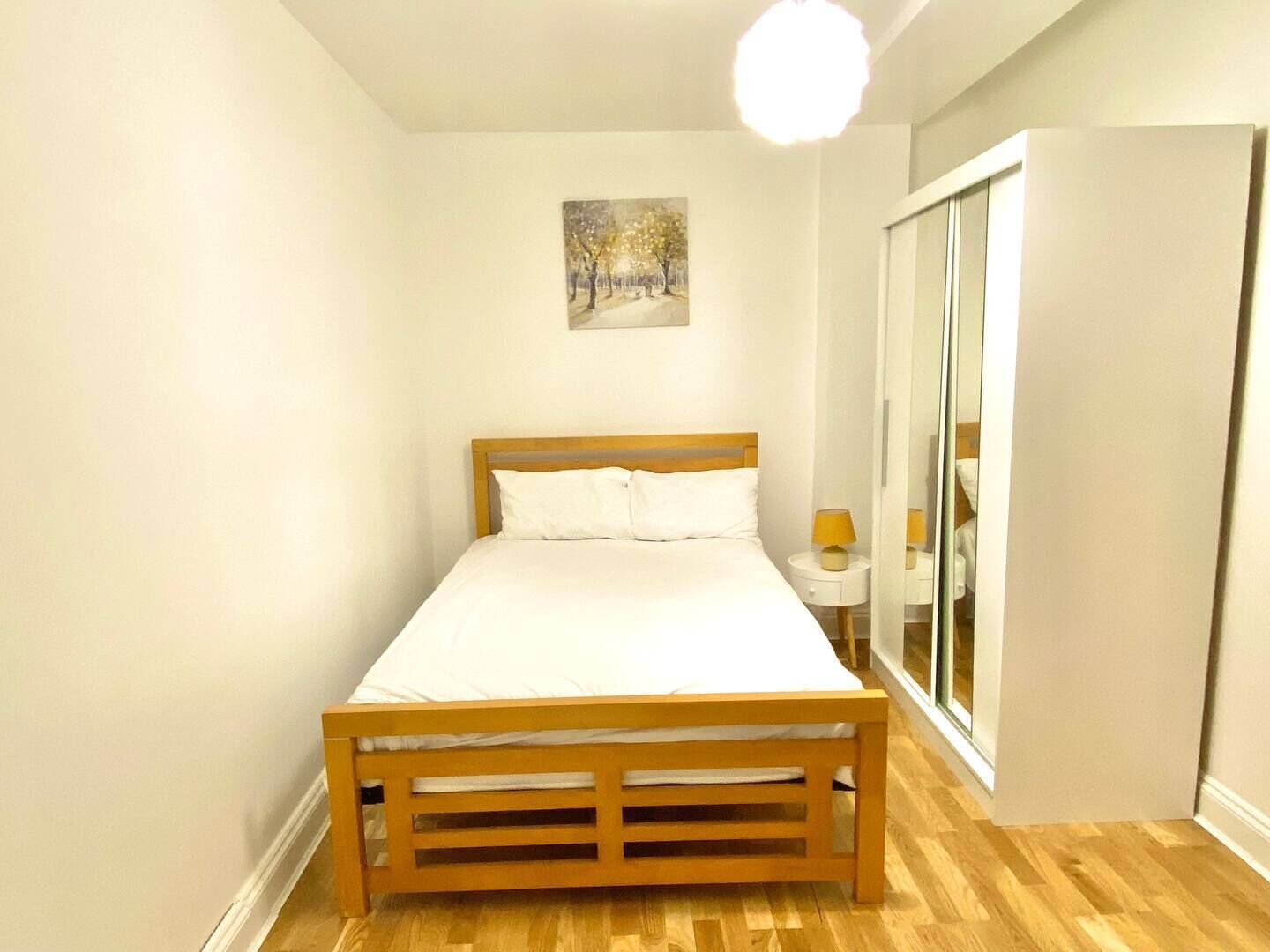 A bedroom with a wooden bed, a bedside table with a lamp, and a wardrobe.