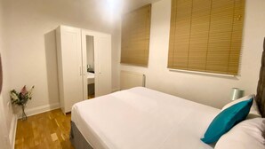 A bedroom with a bed, a wardrobe, a radiator, and a window with blinds. - London apartment

 (London)