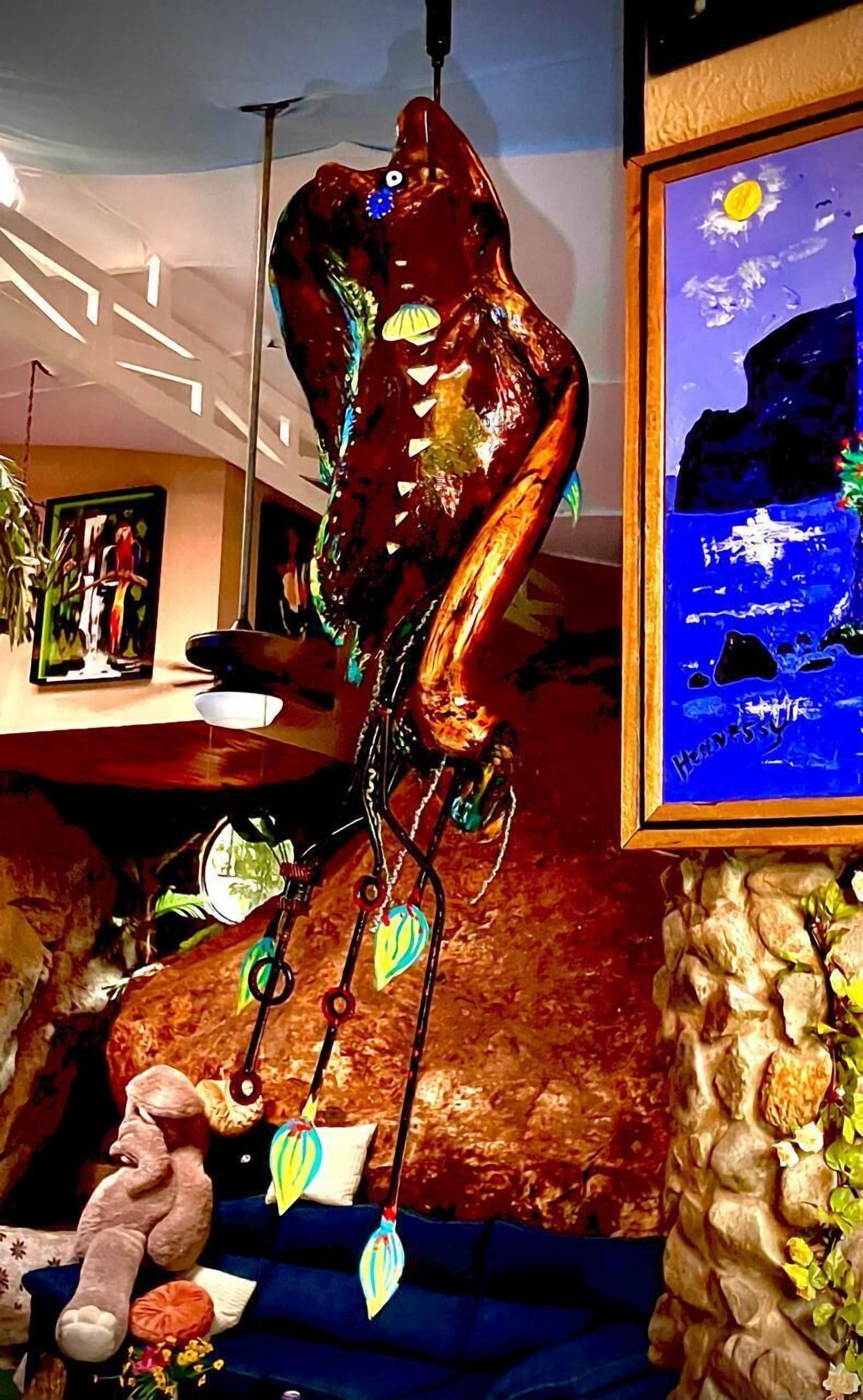 A room with a large abstract sculpture, a framed painting, and a plush toy on a blue sofa.