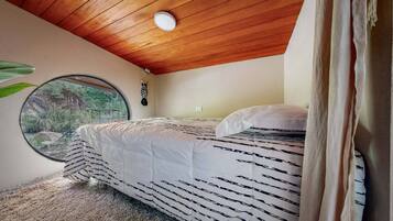 A bedroom with a wooden ceiling, a round window, and a bed with striped bedding.