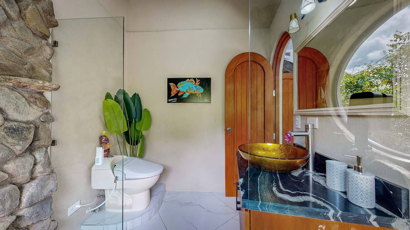 Et badeværelse med stenvæg, toilet, vask med stor kumme og en trædør.