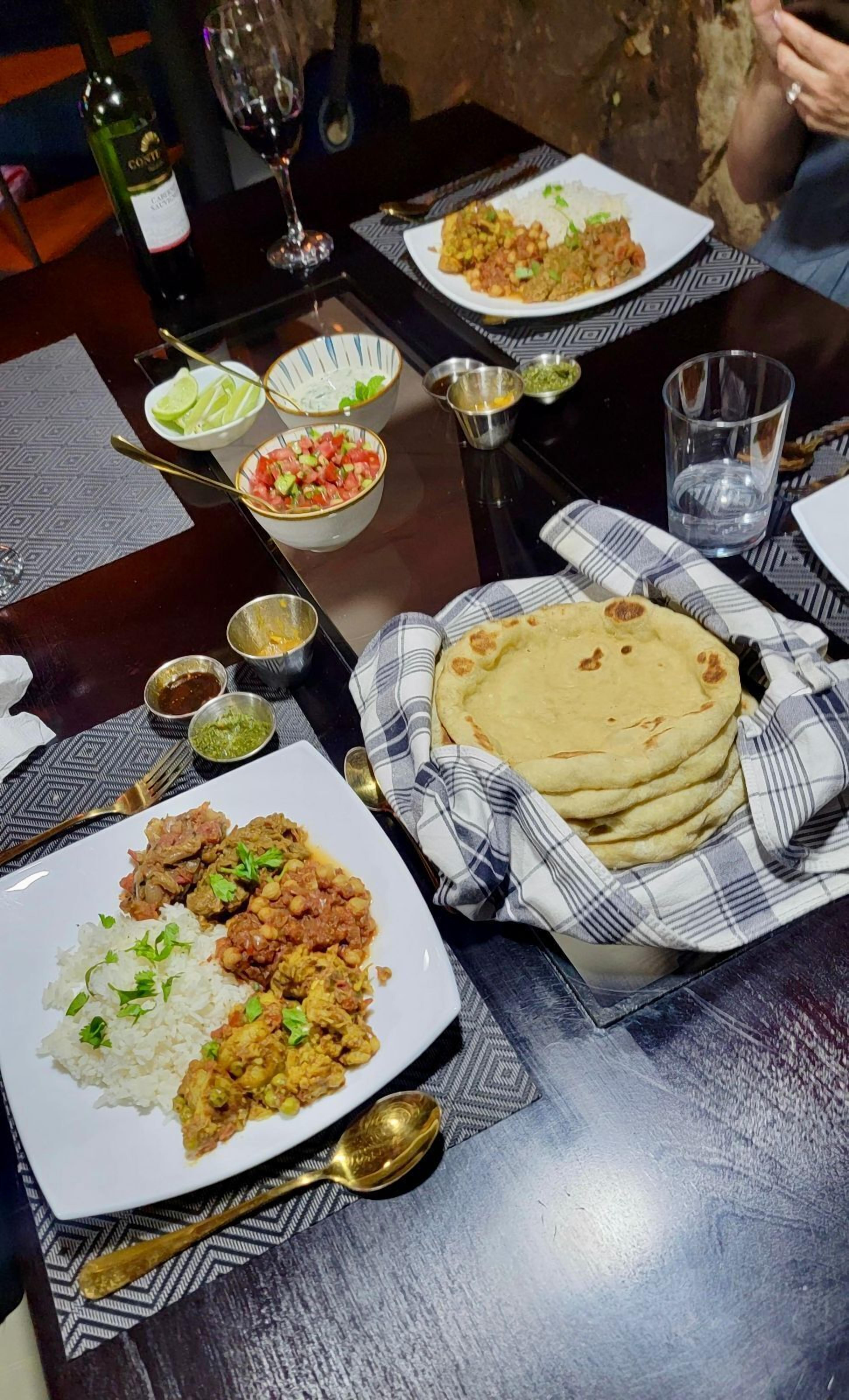 A dining table with plates of food, glasses, and a bottle of wine.