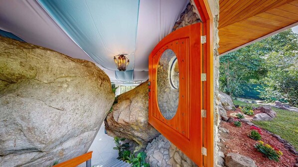 A stone archway leading to a wooden door with a circular window, surrounded by a garden with various plants and a stone wall. - Rocka Verde Retreat (Rivas)