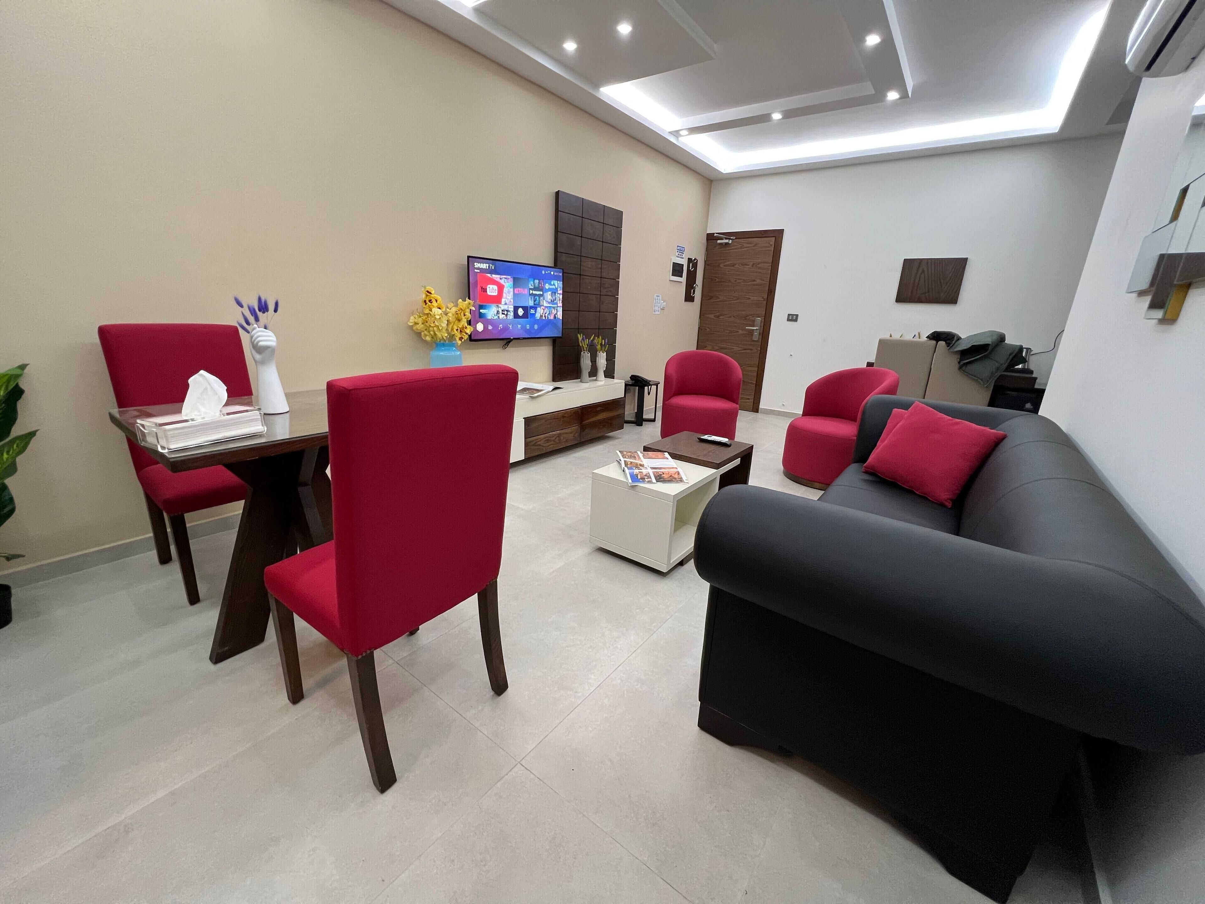 Una sala de estar moderna con un sofá, sillas rojas, una mesa de centro y un televisor.