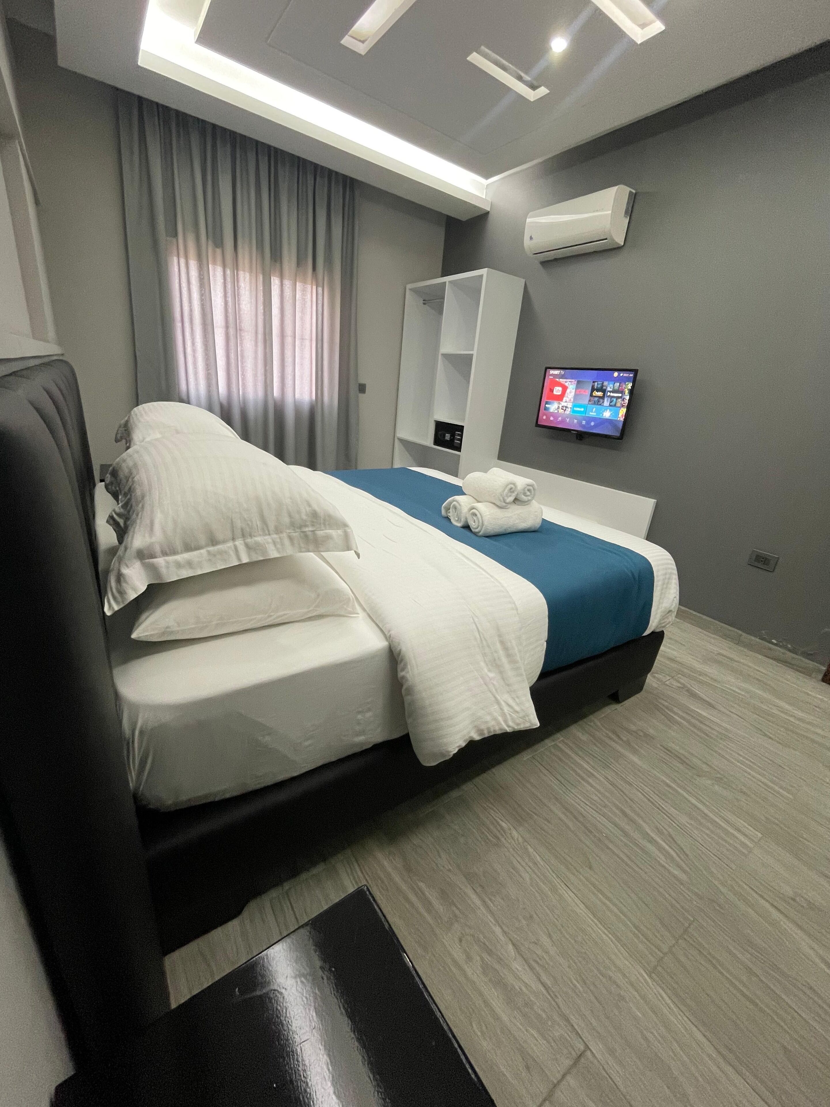 Moderni hotellihuone, jossa on siististi pedattu sänky, seinälle asennettu taulutelevisio ja ilmastointilaite.