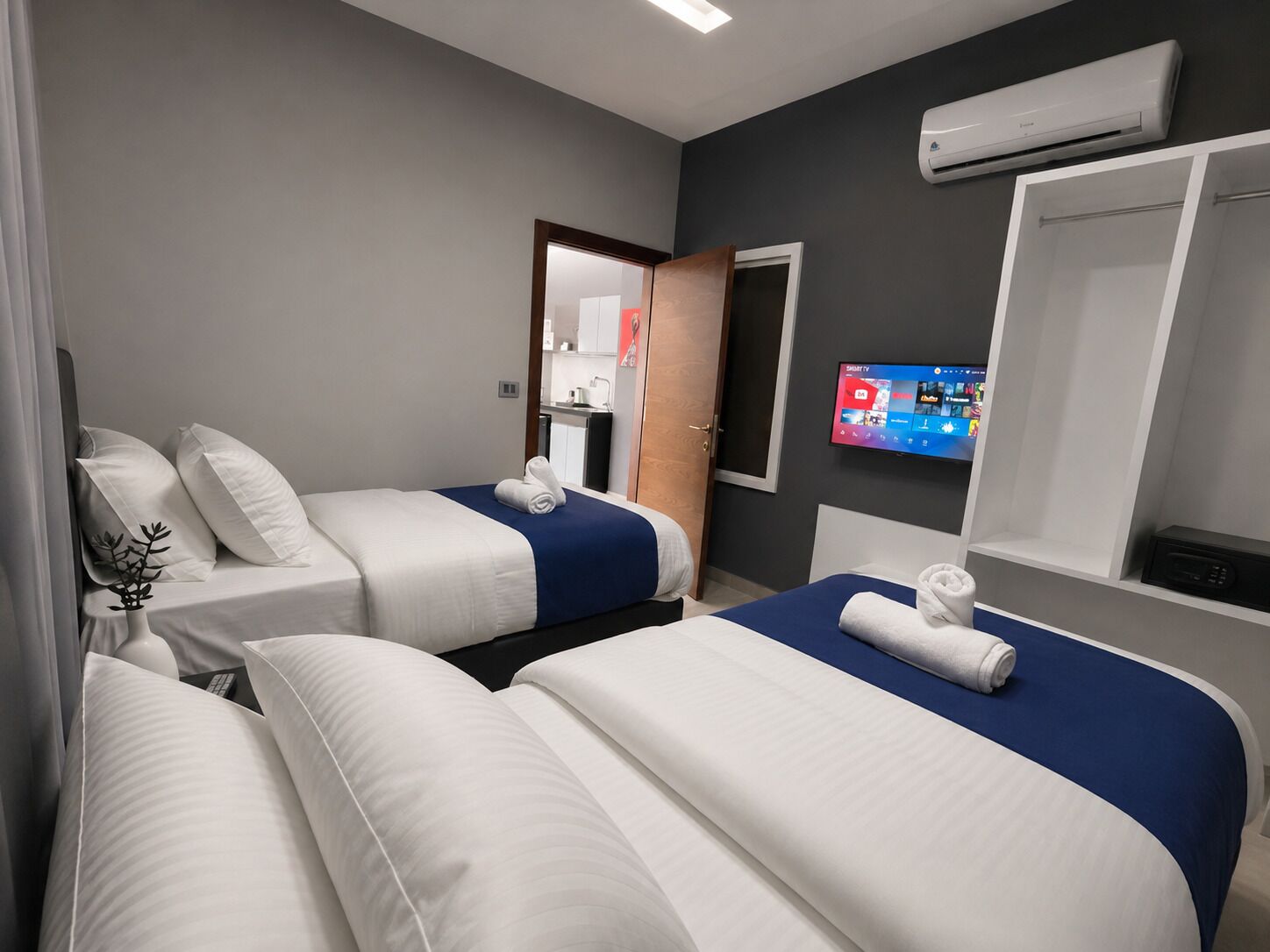 A hotel room with two beds, a TV, and an air conditioning unit.