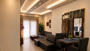 A modern living room with a sofa, a dining table with chairs, a potted plant, and a large mirror. - Matar Residence Hotel Suites (Sabtiyeh)