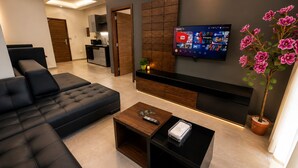 A modern living room with a black sofa, a coffee table, a TV mounted on the wall, and a potted plant. - Matar Residence Hotel Suites (Sabtiyeh)