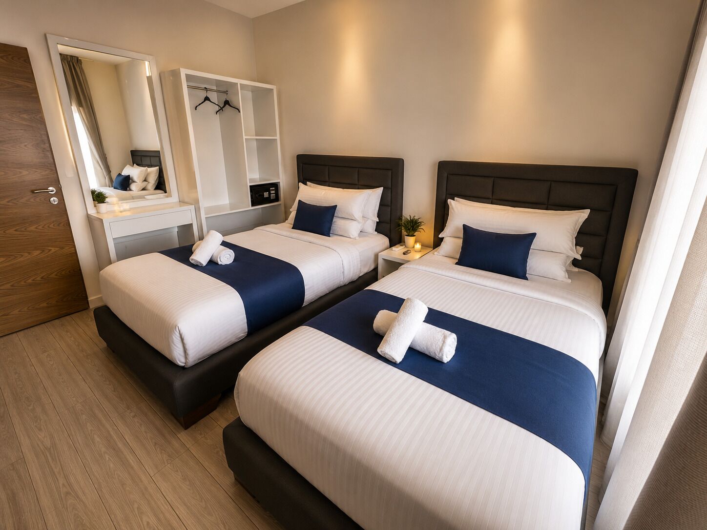 A hotel room with two beds, a wardrobe, a mirror, and a bedside table with a lamp.