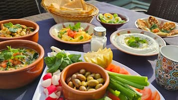 A table with various dishes, including salads, dips, and bread, set on a balcony with a city view.