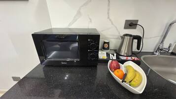 Una cocina con microondas negro, cafetera, fregadero y un bol de fruta sobre la encimera.