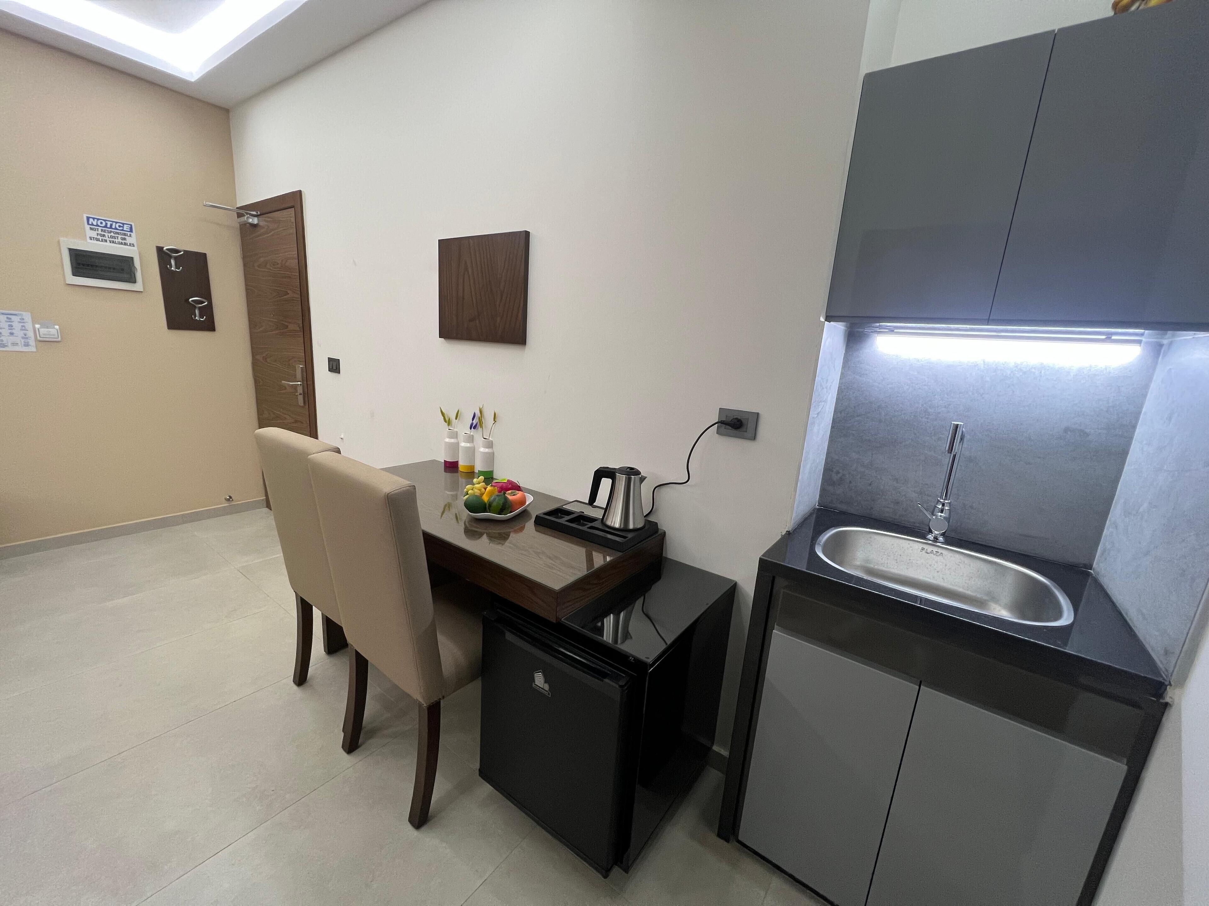 A compact kitchen with a sink, a small refrigerator, and a dining area with a chair and table.