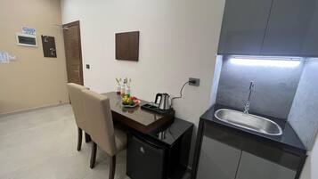A compact kitchen with a sink, a small refrigerator, and a dining area with a chair and table.