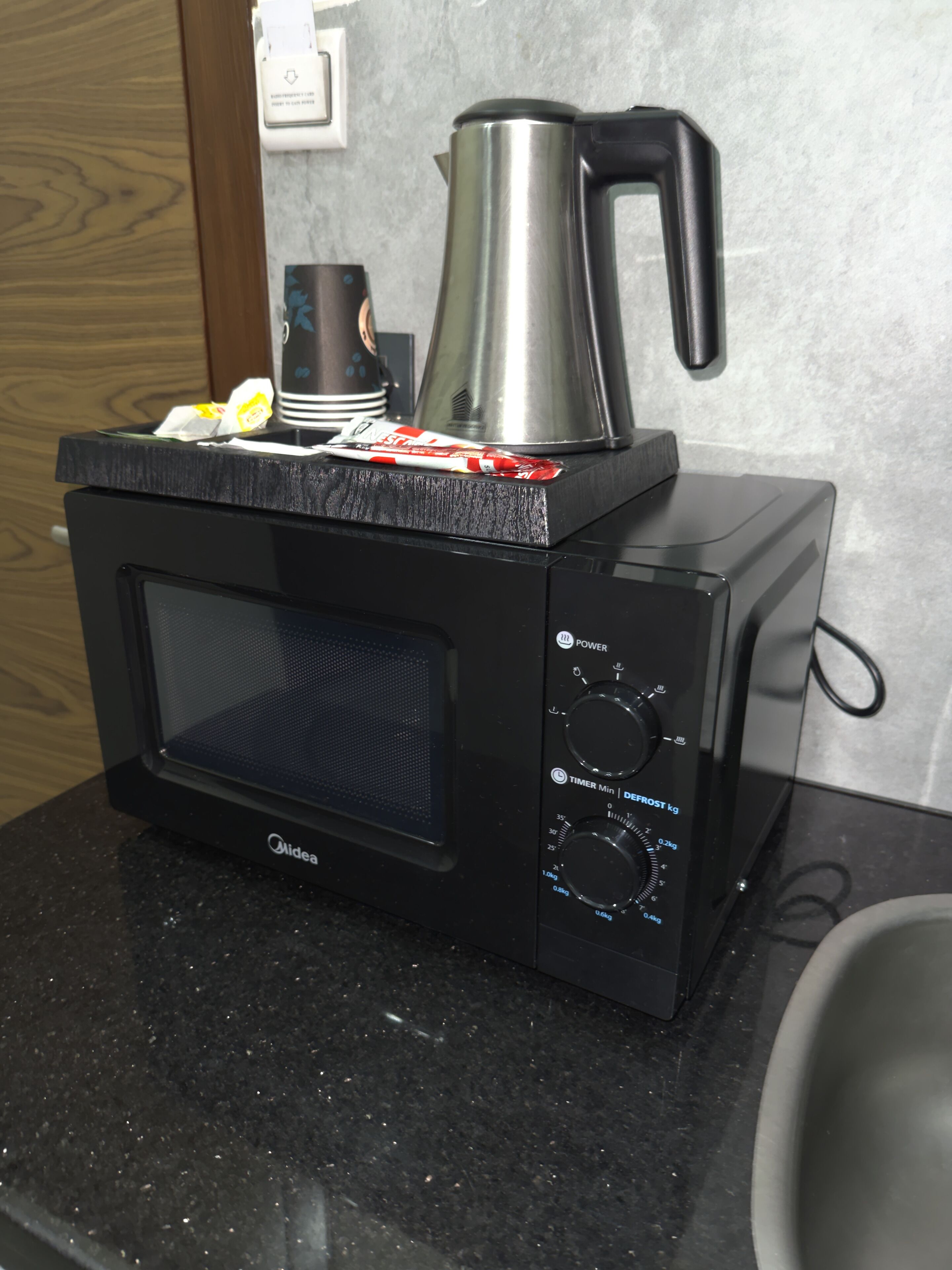 A black microwave oven with a coffee pot on top, placed on a granite countertop.