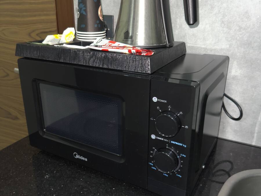 A black microwave oven with a coffee pot on top, placed on a granite countertop.
