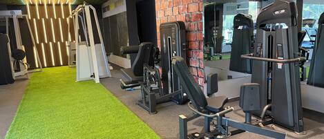 A gym with exercise equipment, green artificial turf, and a brick wall.