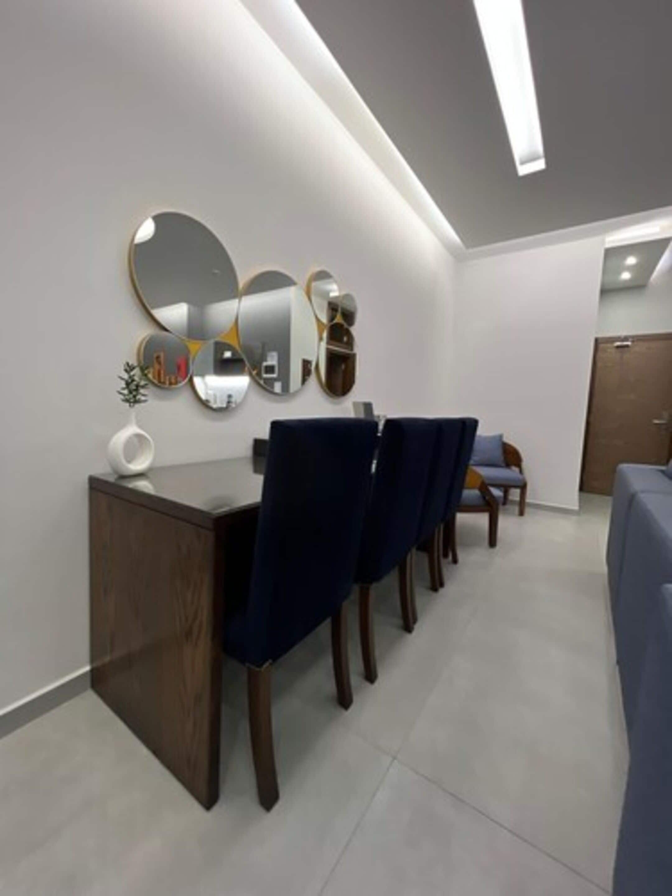 A modern dining area with a wooden table, dark blue chairs, and a wall-mounted mirror.