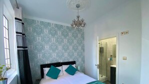 A hotel room with a bed, a chandelier, a shower area, and a window with curtains.