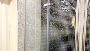 A shower with a glass door, a tiled wall, and a showerhead.