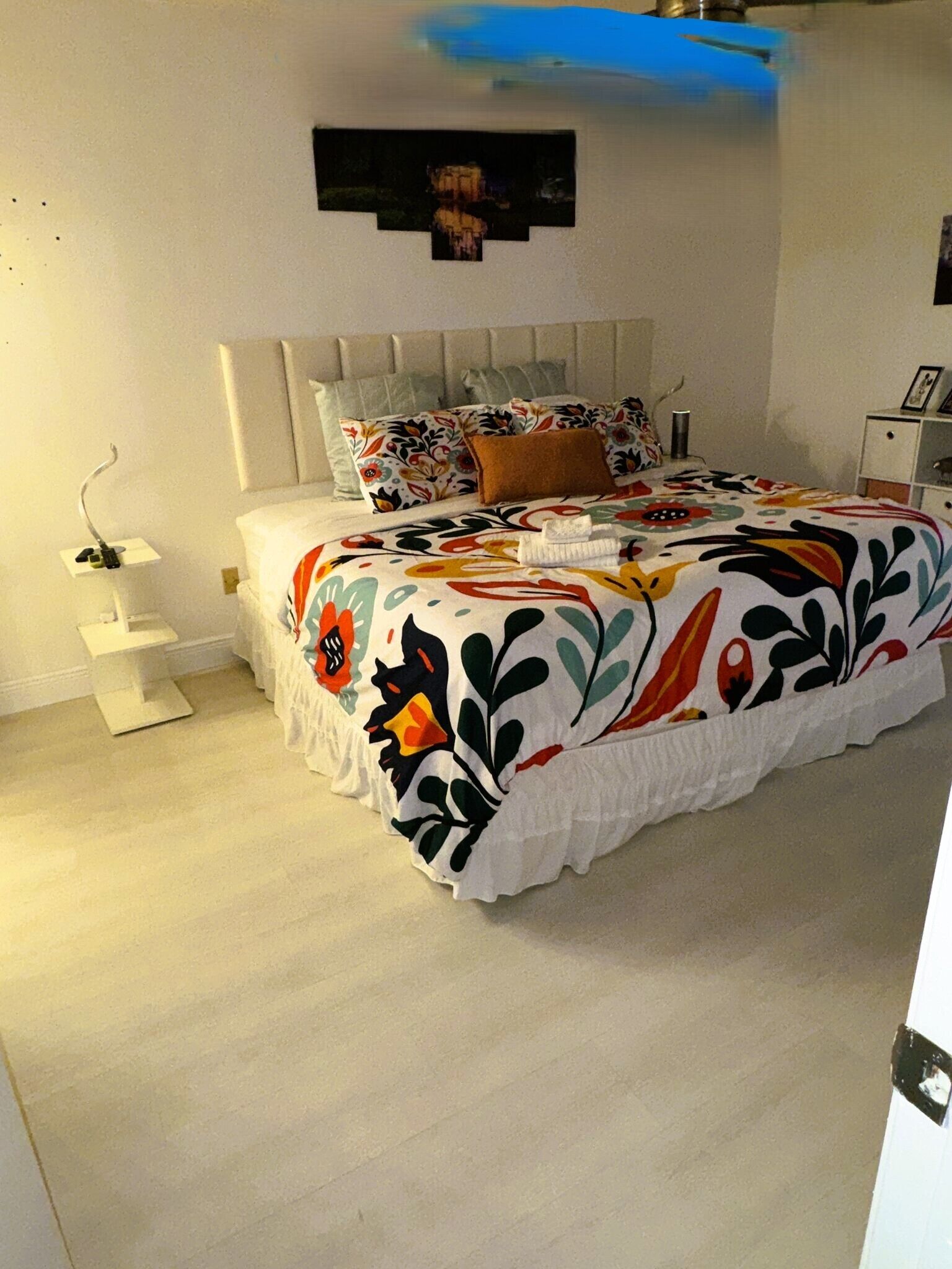 A bedroom with a bed, a bedside table, a nightstand, and a wall-mounted shelf.