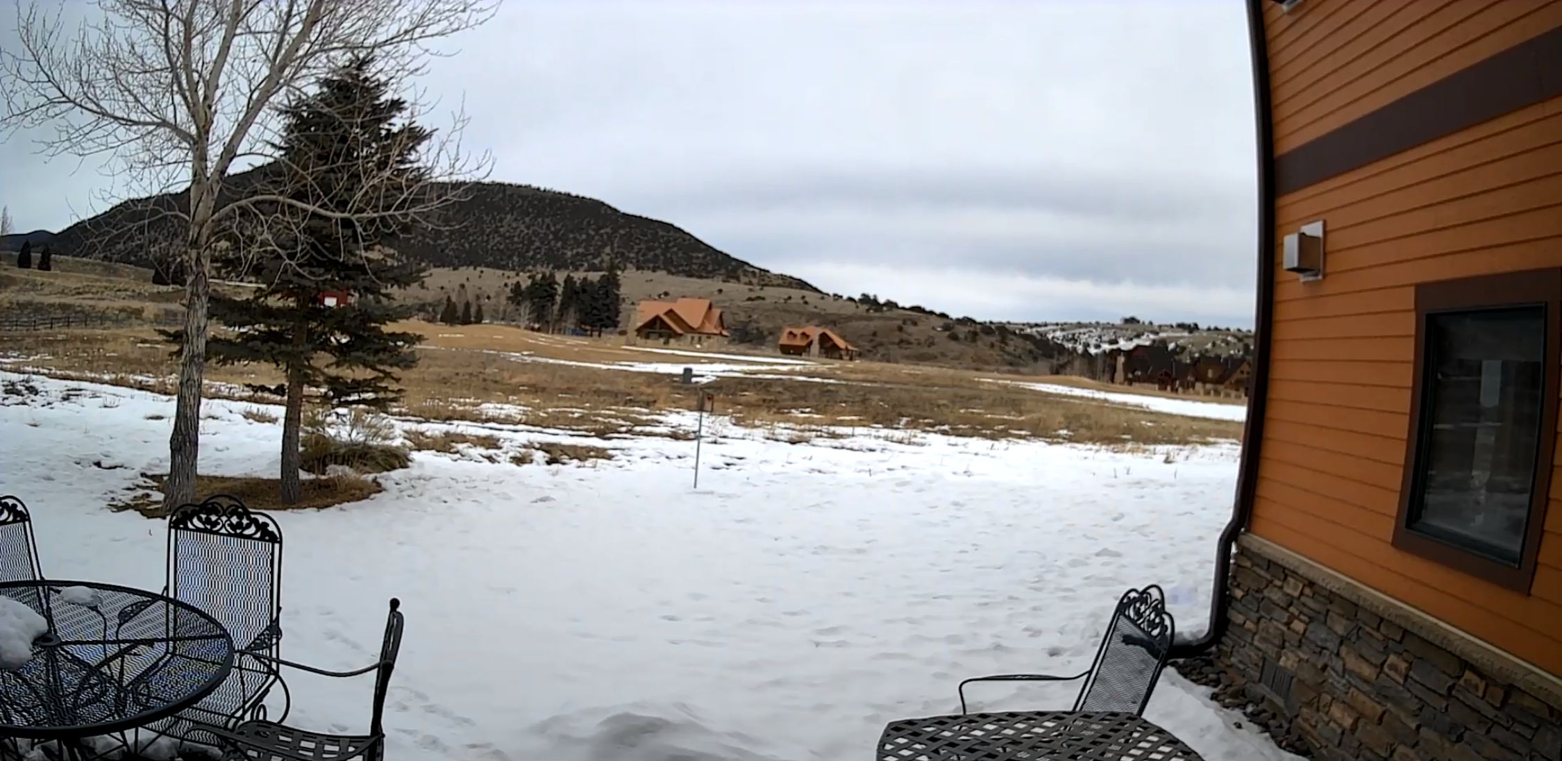 A snowy outdoor area with metal chairs and a building in the background.