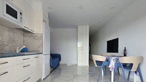 Et moderne køkken med hvide skabe, en mikrobølgeovn og et spiseområde med bord og stole.
