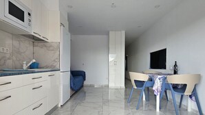 Et moderne køkken med hvide skabe, en mikrobølgeovn og en blå stol ved et spisebord.