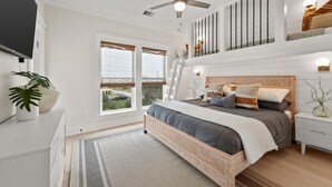 Ein Schlafzimmer mit Bett, Nachttisch, Fernseher, Deckenventilator und Fenster mit Jalousien.