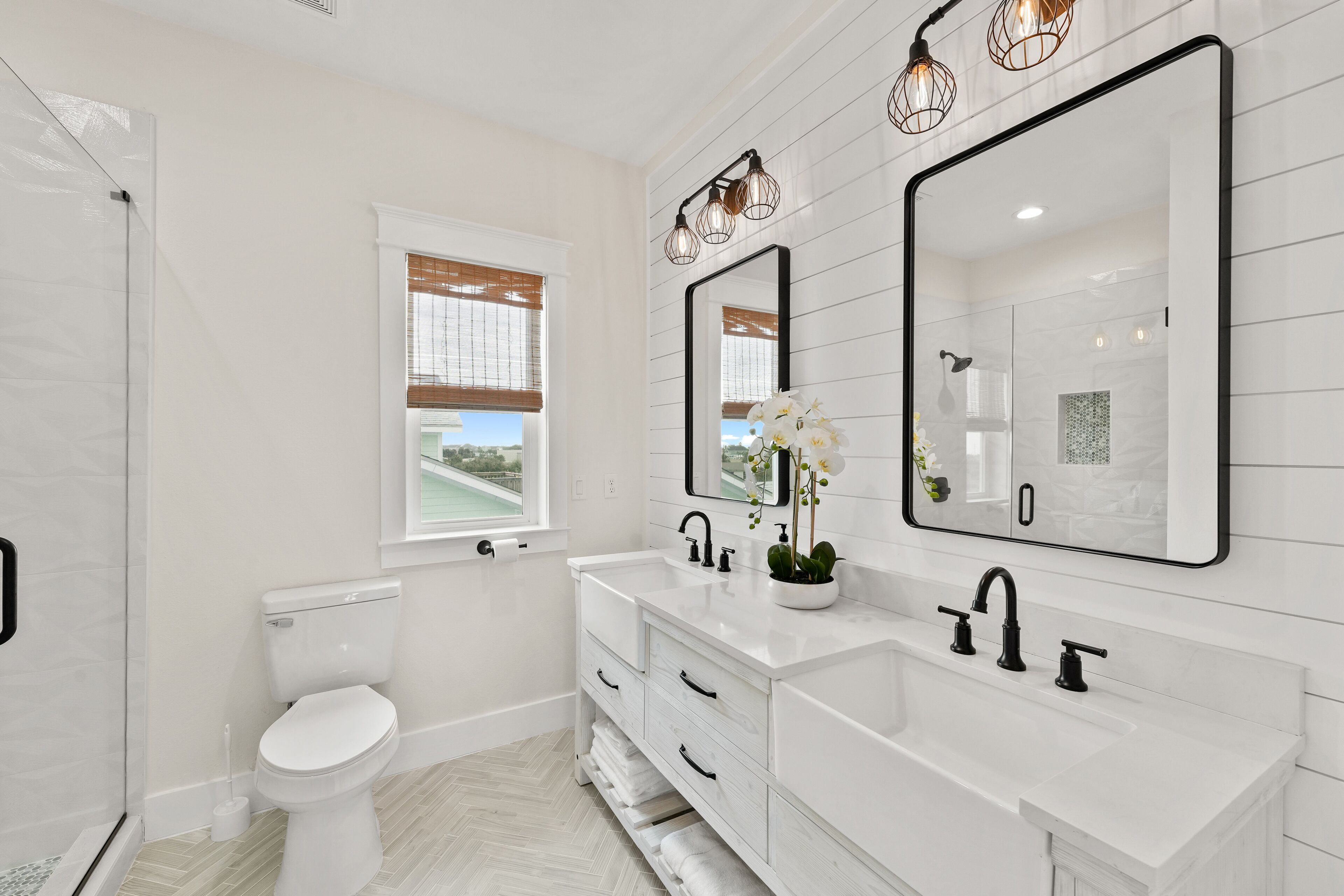 A modern bathroom with white fixtures, a large mirror, and a window with blinds.