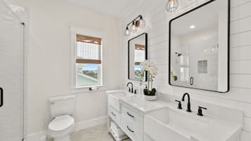 A modern bathroom with white fixtures, a large mirror, and a window with blinds.