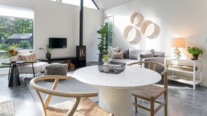 A modern living room with a round table, comfortable seating, a fireplace, and a large window offering a view of the outdoors.
