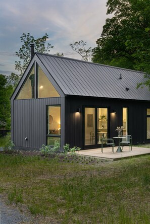 A modern house with a dark exterior, large windows, and a patio area with outdoor seating.