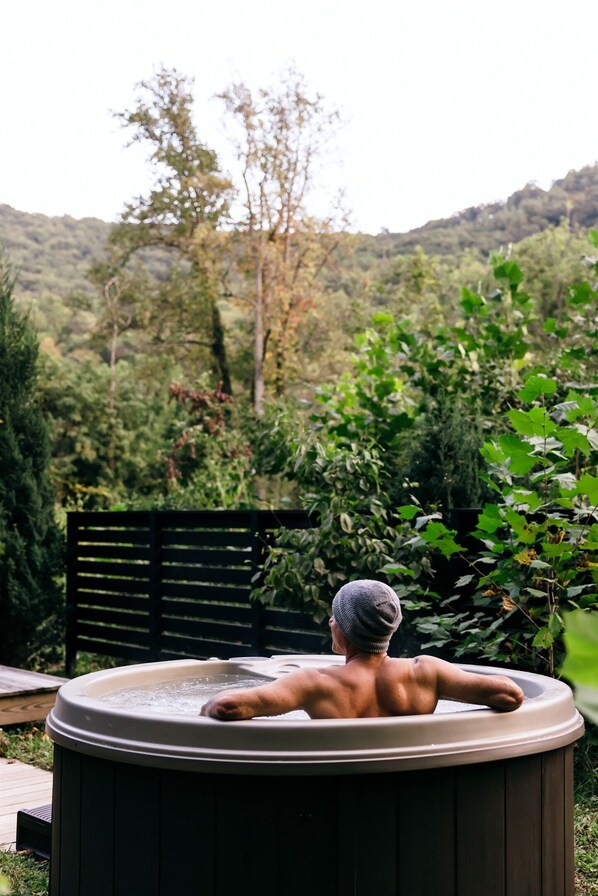 A person relaxing in a hot tub with a view of a forested hillside.