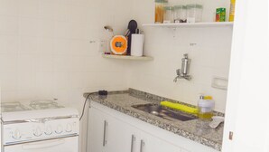 A kitchen with white cabinets, a granite countertop, a stainless steel sink, and a stove. - Refuge for your family (Centro Guarapari)