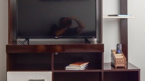 A modern entertainment unit with a flat-screen TV, shelves for books and decorative items, and a small refrigerator. - Refuge for your family (Centro Guarapari)