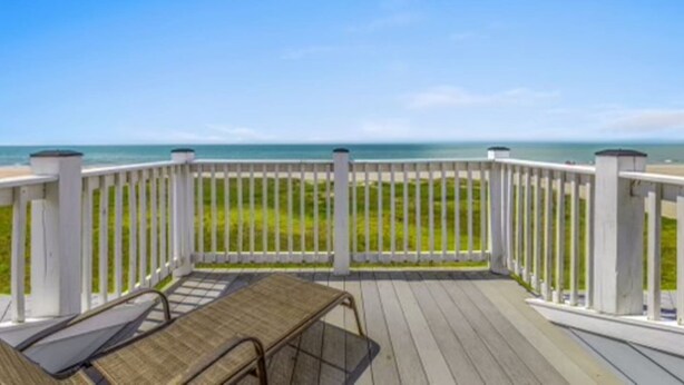Um deck de madeira com mesa e cadeiras, com vista para uma praia e oceano.