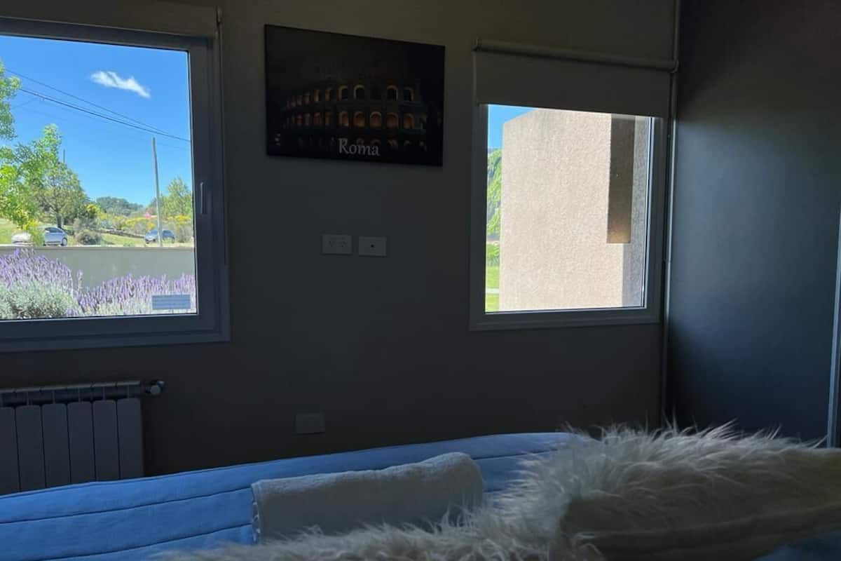 A room with a bed, a window with a view of a road and greenery, and a sign on the wall.