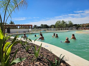Une piscine avec des personnes dans lâeau, entourĂ©e dâune clĂŽture et de vĂ©gĂ©tation.