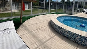 A covered outdoor area with a swimming pool, glass walls, and a thatched structure.