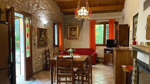 A stone-walled room with a wooden ceiling, a dining table with chairs, a red sofa, a television, and a kitchen area with a stove. - Chalet 'Casa Dell'uliveto' with Mountain View, Wi-Fi and Air Conditioning (Albettone)