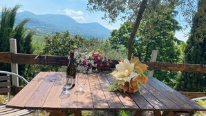 A wooden table with two wine glasses and a bottle, surrounded by a wooden fence, with a mountain view in the background. - Chalet 'Casa Dell'uliveto' with Mountain View, Wi-Fi and Air Conditioning (Albettone)