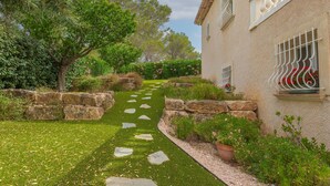 Un sendero en un jardín que conduce a un edificio con muros de piedra y plantas en macetas.