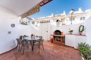 Een terras met een ronde tafel en stoelen, een pizzaoven en potplanten.
