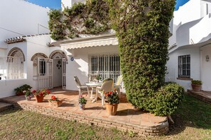 A white building with a patio area featuring a table and chairs, surrounded by potted plants and a large bush. - Apartment 'La Cala Mijas Playa Club' with Sea View, Wi-Fi and Air Conditioning (La Cala de Mijas)