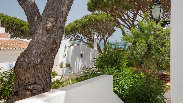 Un edificio bianco con un grande albero sullo sfondo, un lampione e vista sul mare.