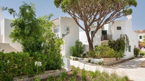 Un edificio bianco con un albero di fronte, un muro in pietra e un cielo sereno.