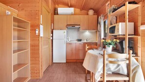 A compact kitchen with wooden cabinets, a refrigerator, a microwave, and a dining table with chairs. - Chalet 'Joli En Bois' with Private Terrace, Wi-Fi & Air Conditioning (Roquebrune-sur-Argens)
