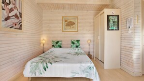 Un dormitorio con cama, paredes de madera, un cuadro enmarcado, una puerta y un termostato.