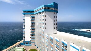 Un hôtel à plusieurs étages, doté d’une façade blanche et de touches de bleu, qui offre une vue sur l’océan.