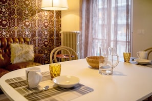 A dining area with a table set for two, a patterned wallpaper, a sofa, and a lamp.